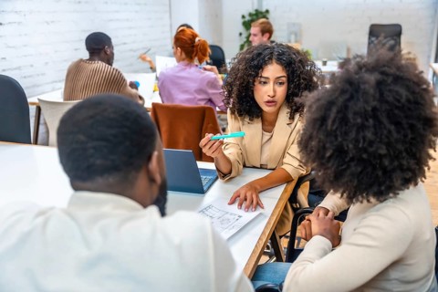 Diverse females and male coworkers discussing data in a coworking meeting room