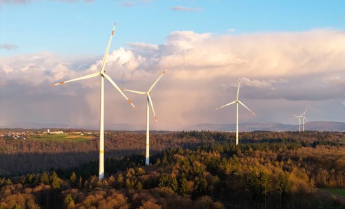 A series of wind turbines in the forest against a dramatic backdrop of clouds in the sky, wind
