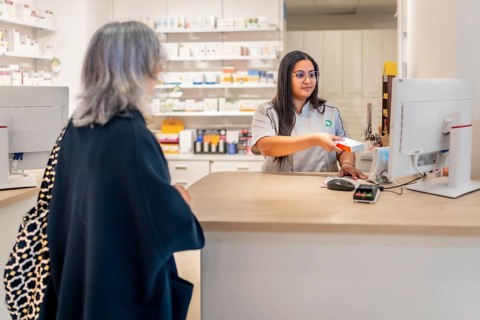 Saleswoman attending a woman in the counter of a pharmacy and checking the price of a medicine
