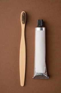 Top view of a bamboo toothbrush and a toothpaste tube on a brown paper background. The image