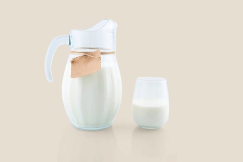 Fresh milk is being poured into a glass from a glass jug with a blank label attached