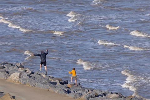 Adult and child running over rocks, sea, waves, surf, The Naze Nature Reserve, Walton-on-the-Naze,