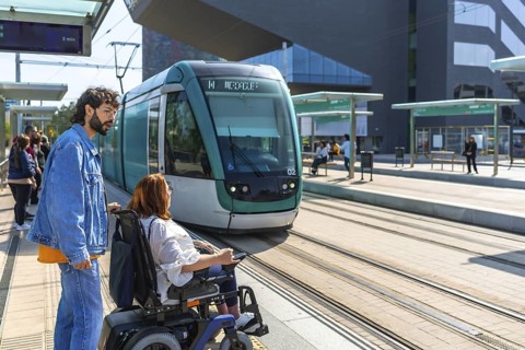 Young man accompanying a woman in a wheelchair waiting for a modern tram to arrive at a station,