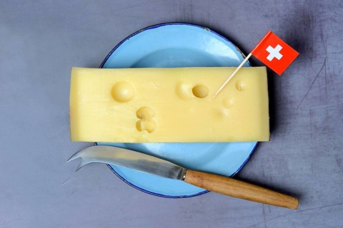 A piece of Swiss Emmental cheese on a plate and the Swiss flag