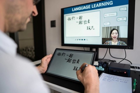 A man learning Mandarin online at home, engaging with a virtual instructor via video call. He
