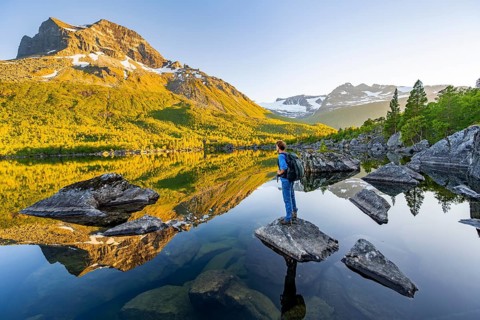 Young man standing on a rock in water, enjoying the landscape, picturesque mountain scenery in the