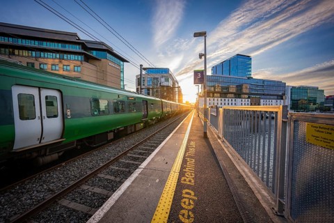 A train at sunset on a platform with modern office buildings in the city, Dockland, Dublin, Ireland