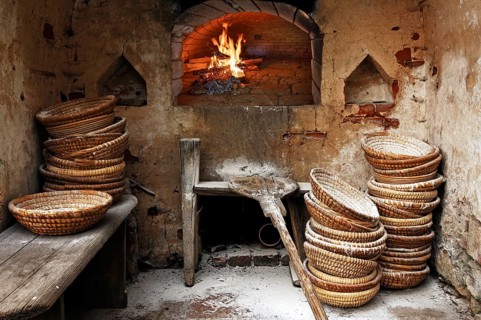 Bread baskets and bread sliders stacked with flour in the bakery, wood-fired fire in the oven,