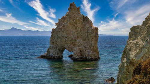 An impressive rock with a hole jutting out of the sea under a lively sky, Aspragremna, White