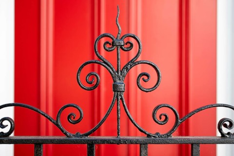 Close-up of an elegant curved metal grid in the foreground and red door in the background, Chelsea,