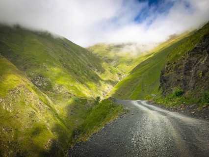 Scenic mountain gravel road in Tusheti region surrounded by foggy caucasus nature.Georgia