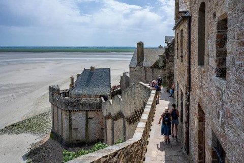 Tourists on the historic rampart of the medieval fortress wall on Mont-Saint-Michel at low tide
