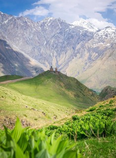 Historical Gergeti trinity church on top of the hill surounded by green nature and mountain in the