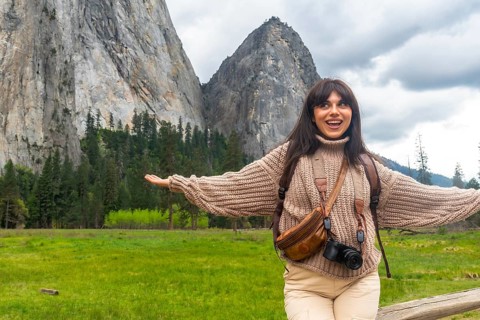Happy woman with arms outstretched in a lush green yosemite meadow, facing el capitan and soaking