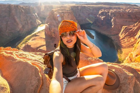 Young woman takes a sunset selfie at horseshoe bend overlooking the winding colorado river through