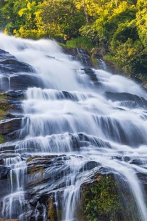 Mae Ya waterfall with cascading flowing water surrounded by lush tropical vegetation, near Doi
