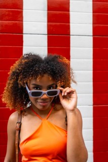 Confident young woman posing with style, adjusting her sunglasses with a playful expression against