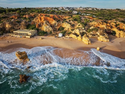 Drone view of waves curling along the beach below golden limestone cliffs at Praia de Sao Rafael