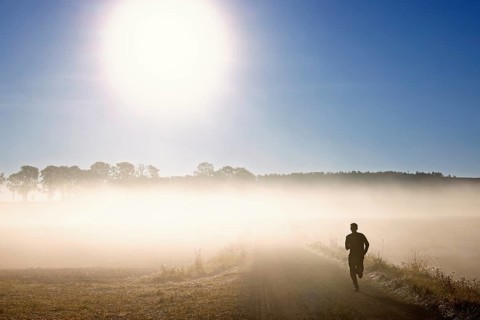Lone runner running along a dirt path in a misty rural landscape during sunrise