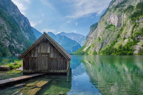Traditional wooden boathouse sitting on the transparent turquoise water of Obersee lake, Bavarian