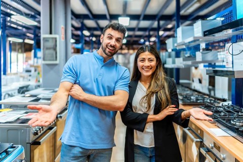 Smiling man and woman standing together in an appliance store showroom, welcoming potential buyers