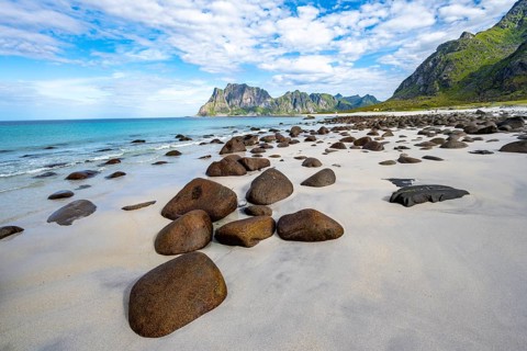 Rocks on the sandy beach of Uttakleiv, coast and blue sea, rocky mountain peaks, Vestvågøya,