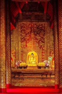 Gilded seated Buddha statue in a public prayer hall in the Wat Phra Singh Buddhist temple complex,