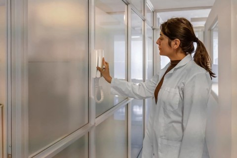 Young female scientist in white lab coat using a wall-mounted intercom handset in a bright