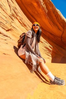 Young woman with a backpack and sunglasses smiling while sitting on the sandstone ground inside