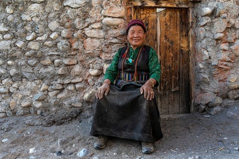 Friendly elderly woman in traditional clothing sitting in front of wooden door, Tangge, Mustang,