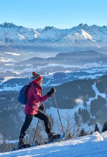 Sportive senior woman hiking with snow shoes in the snowy Allgaeu Alps above Lake Alosee,