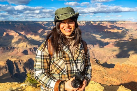 Woman traveler smiling enjoying the vast grand canyon landscape while holding her camera, capturing