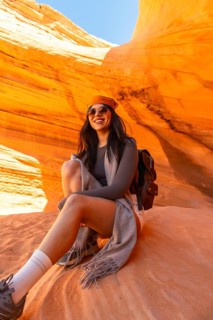 Young woman smiling and sitting on a textured orange sandstone rock formation, exploring the