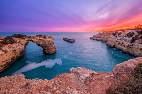 Dramatic sunset view of Arco de Albandeira at Praia de Albandeira in Algarve, Portugal, with pink