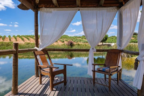 Two wooden chairs in a pavilion with curtains standing over a calm lake, Pedrógão, Beja, Portugal