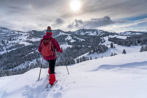 Nice and active senior woman hiking with snowshoes in deep powder snow in the Allgau alps,