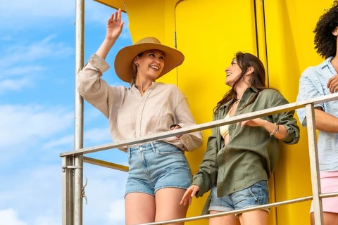 Group of diverse happy young women enjoying sunny summer vacation, standing on a bright yellow