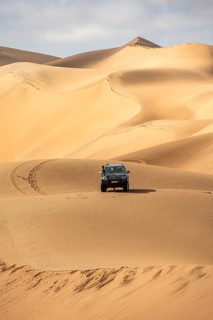 Off-road vehicle between sand dunes, sea of dunes, sandy desert, impressive desert landscape, Namib