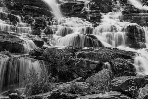 Mae Ya waterfall with cascading flowing water framed by lush tropical vegetation, black and white
