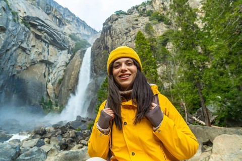 Woman hiker wearing a yellow jacket and beanie smiling at the camera, enjoying the natural beauty
