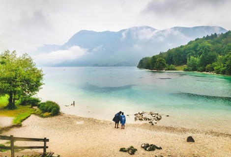 Male and female is standing by the Bohinj lake and looking tothe lake while its raining.Slovenia