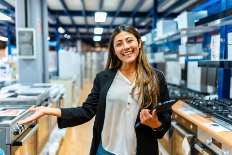 Confident saleswoman smiling while holding a digital tablet and gesturing towards kitchen