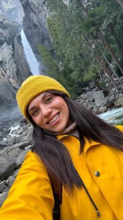 Woman in a yellow jacket and beanie smiles for a selfie while hiking at yosemite national park,