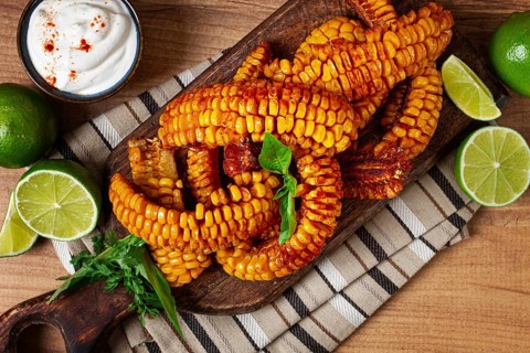 Corn ribs, with cream sauce, spices and lime, appetizer, on a wooden cutting board, homemade, no