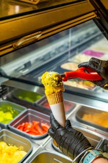 Person wearing black latex gloves serving creamy yellow ice cream with sprinkles into a crispy
