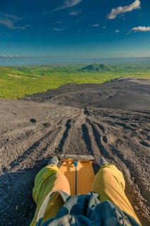View of a person on Cerro Negro riding a sandboard. Person sandboarding on Cerro Negro, Nicaragua