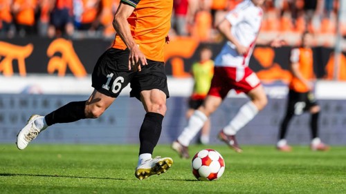 Soccer player in orange jersey number 16 running toward ball on green field during match, real