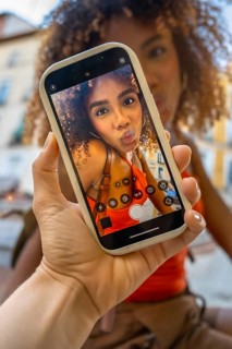 Hand holding a smartphone displaying a confident young woman with curly hair taking a kissy face