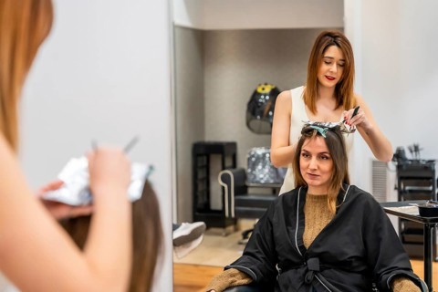 Professional hairdresser carefully applying hair dye with foil for highlights on a client's hair,