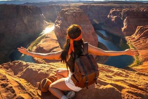 Woman with backpack raising arms in freedom and joy, admiring the breathtaking horseshoe bend